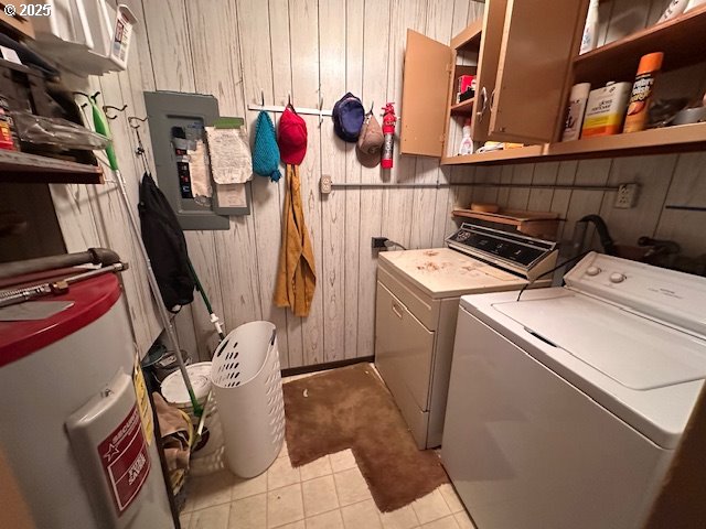 clothes washing area with water heater, independent washer and dryer, wood walls, and light tile patterned flooring