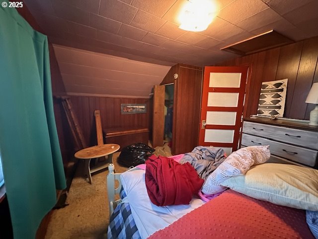 bedroom with carpet flooring, wood walls, and vaulted ceiling