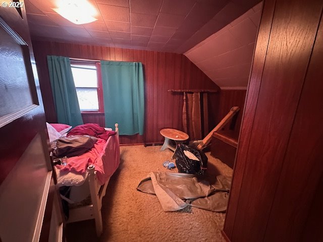 bedroom featuring lofted ceiling, wood walls, and carpet flooring