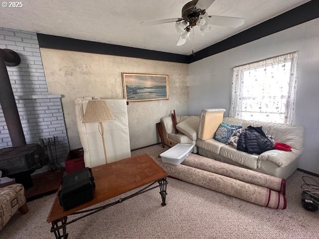 living room featuring ceiling fan, a textured ceiling, a wood stove, and carpet flooring