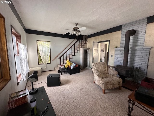 carpeted living room with ceiling fan, a wood stove, and a textured ceiling