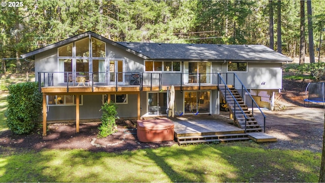 rear view of house featuring stairs, a trampoline, a wooden deck, and a lawn