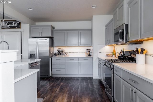 kitchen featuring stainless steel appliances, gray cabinets, backsplash, dark wood-type flooring, and light stone counters