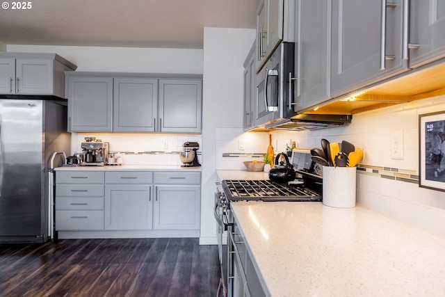 kitchen featuring stainless steel appliances, gray cabinetry, light stone countertops, decorative backsplash, and dark wood-style floors