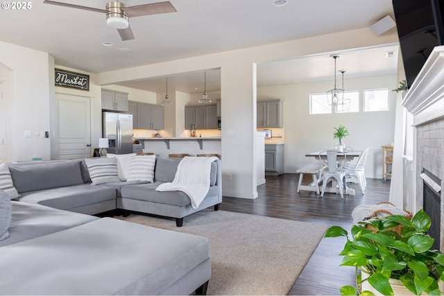 living area featuring a ceiling fan, dark carpet, a fireplace, dark wood-style floors, and a chandelier