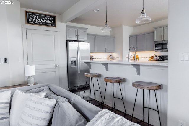 kitchen with appliances with stainless steel finishes, gray cabinetry, a kitchen bar, light countertops, and beam ceiling