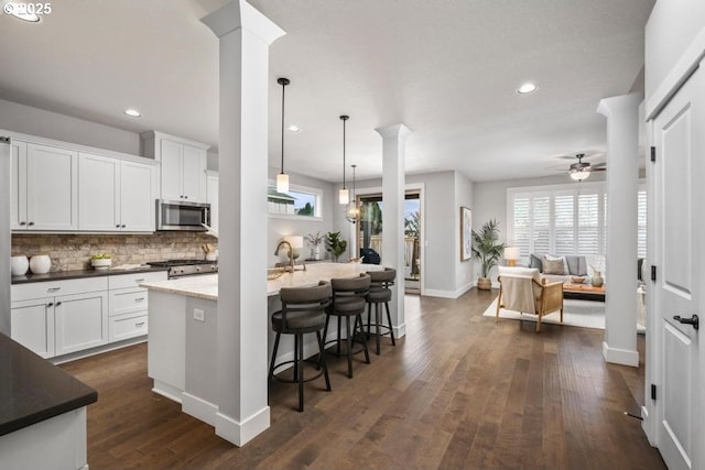 kitchen with ornate columns, appliances with stainless steel finishes, tasteful backsplash, white cabinets, and hanging light fixtures