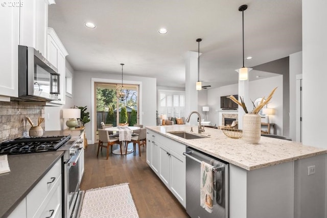 kitchen with appliances with stainless steel finishes, a kitchen island with sink, hanging light fixtures, and white cabinets