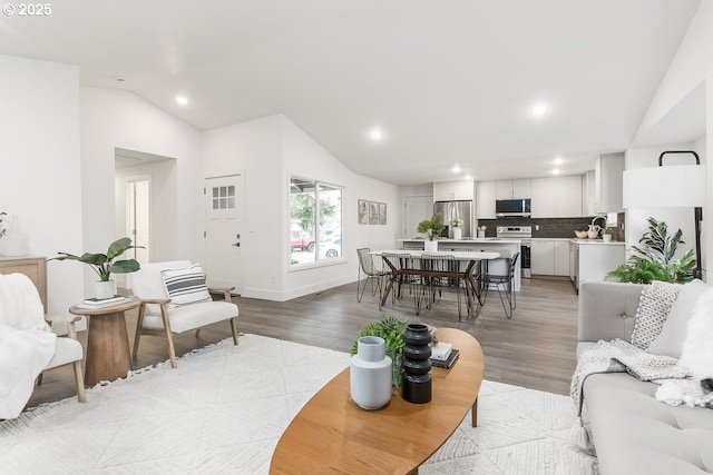 living room with light wood-type flooring, sink, and vaulted ceiling