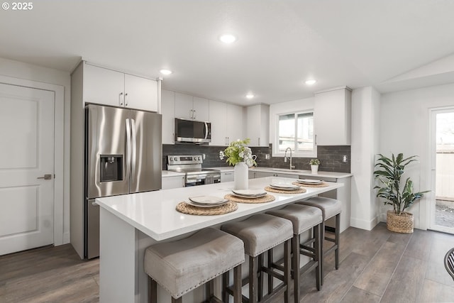 kitchen featuring white cabinets, dark hardwood / wood-style floors, a kitchen island, a kitchen bar, and stainless steel appliances