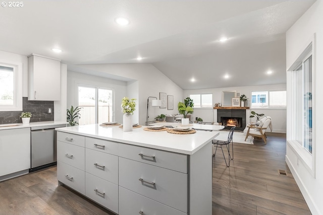 kitchen with decorative backsplash, dark hardwood / wood-style flooring, dishwasher, a kitchen island, and lofted ceiling