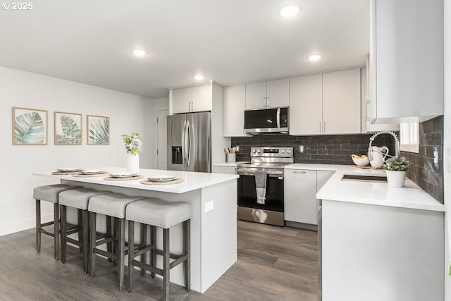 kitchen with dark wood-type flooring, sink, a kitchen bar, white cabinetry, and stainless steel appliances