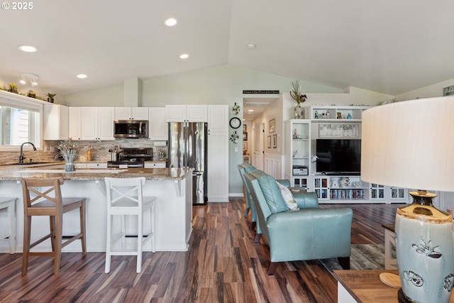 kitchen featuring appliances with stainless steel finishes, a sink, light stone countertops, vaulted ceiling, and dark wood finished floors