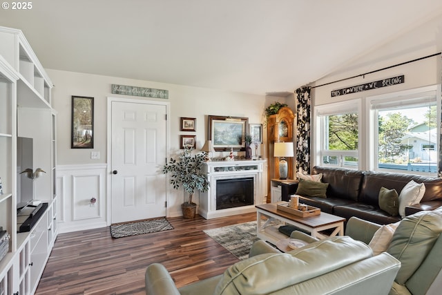 living area with dark wood finished floors, vaulted ceiling, a fireplace, and a wainscoted wall