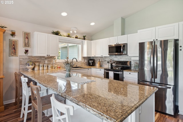 kitchen with stainless steel appliances, tasteful backsplash, a peninsula, vaulted ceiling, and white cabinetry