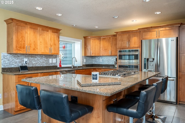 11782 SE 108th Ave, Happy Valley, OR 97086 - kitchen featuring appliances with stainless steel finishes, a kitchen island, tasteful backsplash, a kitchen breakfast bar, and stone countertops