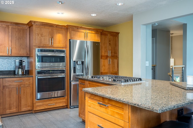 11782 SE 108th Ave, Happy Valley, OR 97086 - kitchen with stainless steel appliances, brown cabinets, light stone countertops, recessed lighting, and backsplash