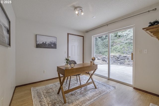 home office with a textured ceiling, light wood-type flooring, and baseboards