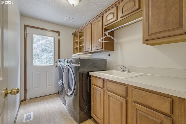 laundry area with a sink, visible vents, independent washer and dryer, light wood-type flooring, and cabinet space