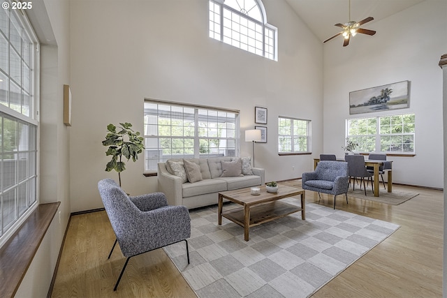 living room featuring baseboards, ceiling fan, light wood-type flooring, and a healthy amount of sunlight