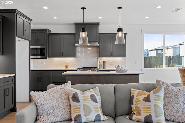 kitchen with pendant lighting, light hardwood / wood-style flooring, a center island, built in appliances, and decorative backsplash