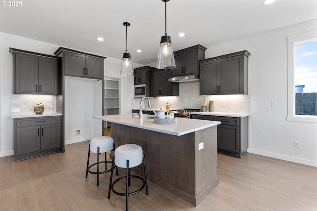 kitchen with pendant lighting, sink, appliances with stainless steel finishes, a kitchen island with sink, and light hardwood / wood-style floors