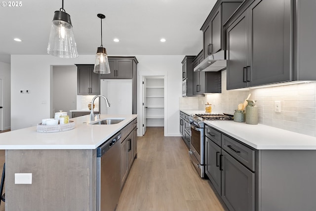 kitchen with sink, decorative light fixtures, light wood-type flooring, stainless steel appliances, and a kitchen island with sink