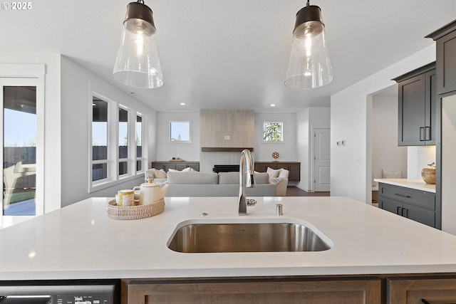 kitchen with pendant lighting, sink, dishwasher, a kitchen island with sink, and a fireplace