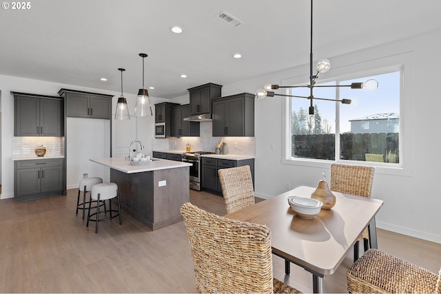 kitchen with sink, tasteful backsplash, hanging light fixtures, stainless steel range with gas stovetop, and a kitchen island with sink