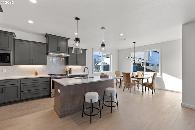 kitchen featuring sink, hanging light fixtures, stainless steel range, a center island with sink, and built in microwave