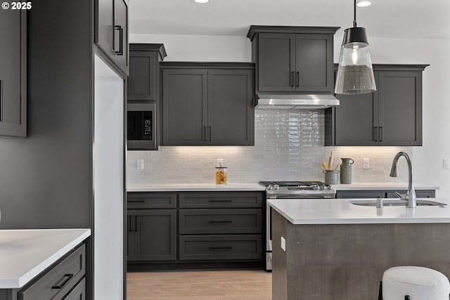 kitchen with sink, light wood-type flooring, appliances with stainless steel finishes, pendant lighting, and decorative backsplash