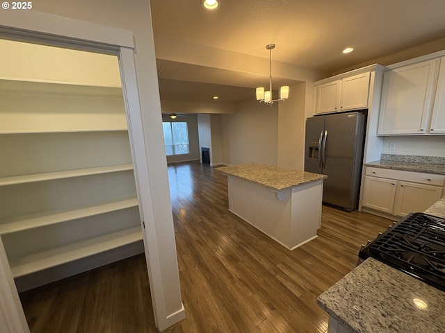 kitchen with light stone countertops, stainless steel fridge, decorative light fixtures, white cabinets, and a kitchen island