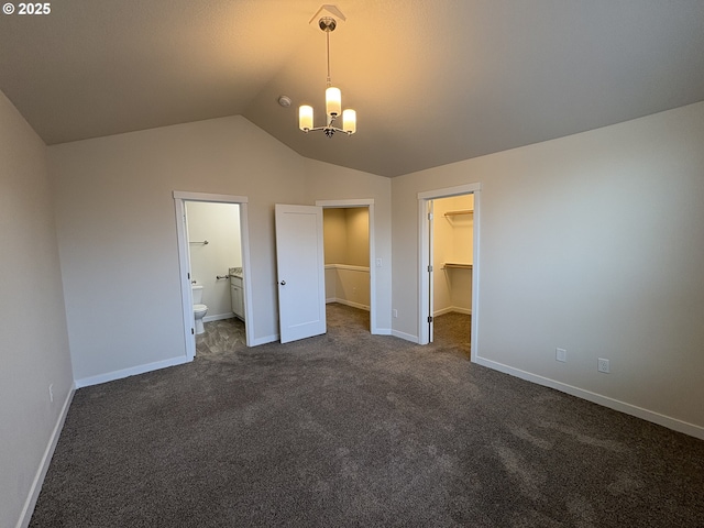 unfurnished bedroom featuring dark carpet, ensuite bath, vaulted ceiling, a spacious closet, and a closet