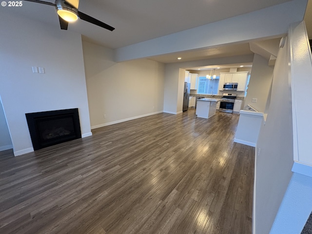 unfurnished living room featuring ceiling fan with notable chandelier, sink, and dark wood-type flooring