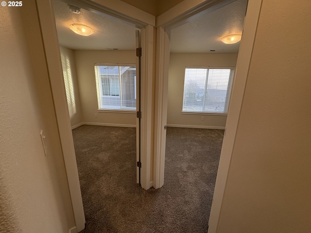 hallway featuring a textured ceiling and dark carpet