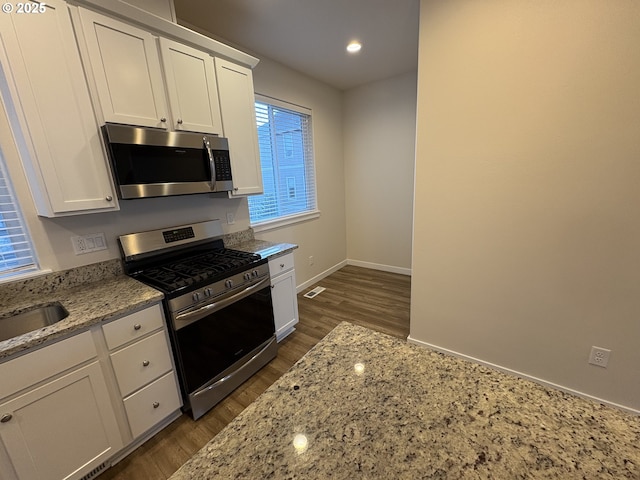 kitchen with light stone countertops, appliances with stainless steel finishes, dark hardwood / wood-style flooring, sink, and white cabinets