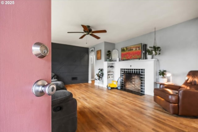 living room featuring a tiled fireplace, a ceiling fan, and wood finished floors