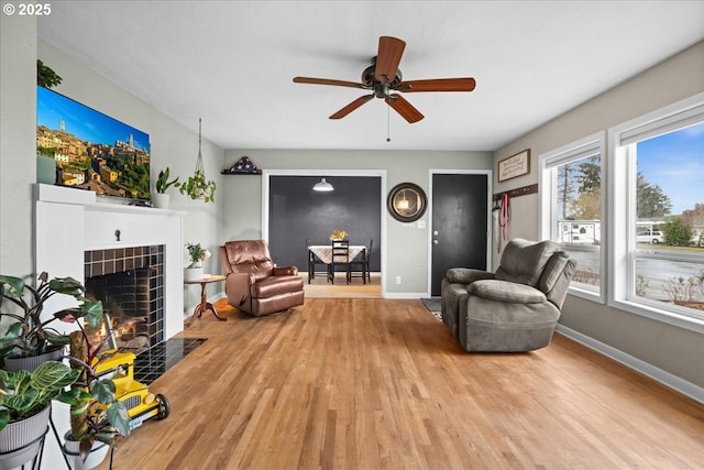 sitting room featuring a tiled fireplace, a ceiling fan, baseboards, and wood finished floors