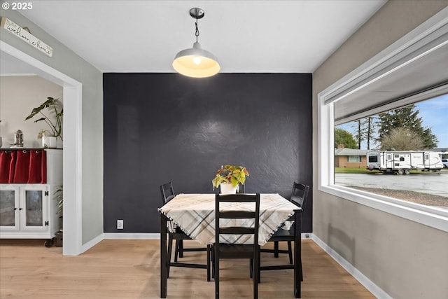 dining space with baseboards, an accent wall, and light wood-style floors