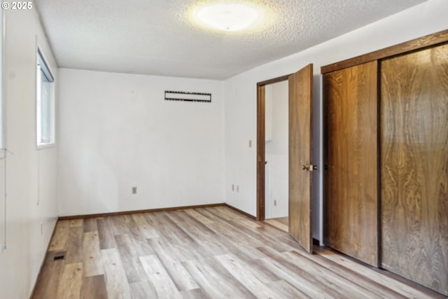 unfurnished bedroom featuring a textured ceiling, visible vents, baseboards, a closet, and light wood finished floors