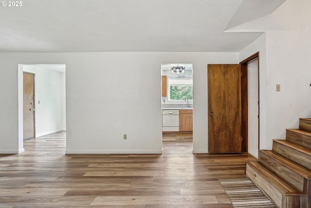 unfurnished room featuring a sink, baseboards, stairway, and wood finished floors