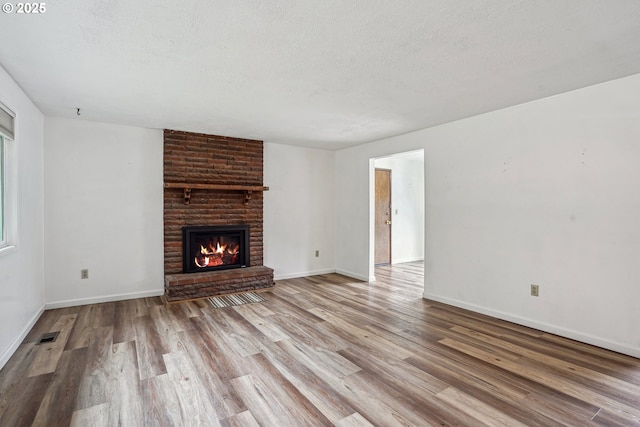 unfurnished living room with a textured ceiling, a brick fireplace, and wood finished floors