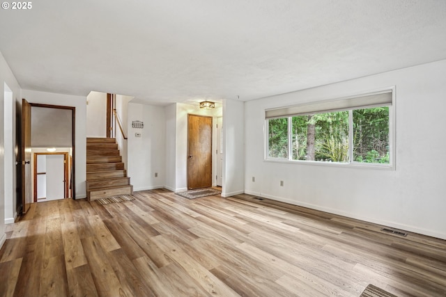 interior space with light wood-style flooring, visible vents, stairway, and baseboards