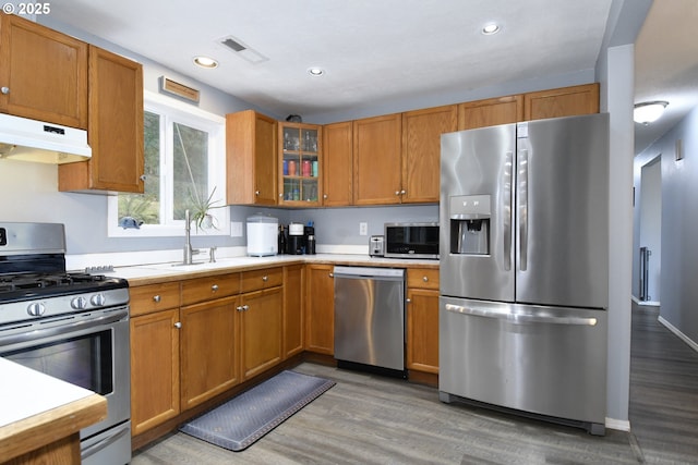 kitchen with under cabinet range hood, a sink, stainless steel appliances, light wood-style floors, and light countertops