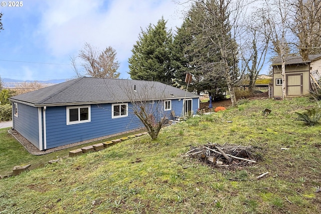 rear view of property with a shingled roof, an outdoor fire pit, a lawn, a storage shed, and an outbuilding