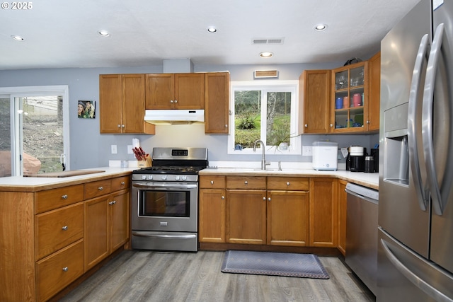 kitchen featuring visible vents, under cabinet range hood, brown cabinets, a peninsula, and stainless steel appliances