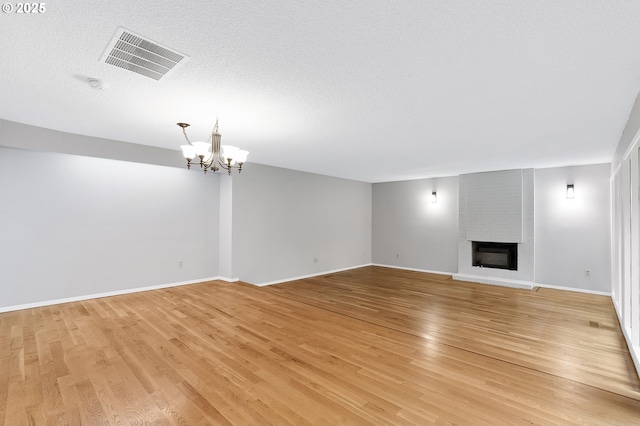 unfurnished living room featuring an inviting chandelier, light hardwood / wood-style flooring, a textured ceiling, and a fireplace