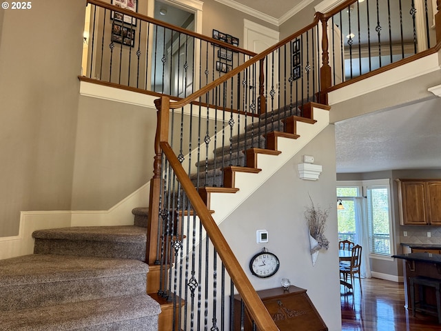 stairs featuring wood finished floors, ornamental molding, a high ceiling, and baseboards