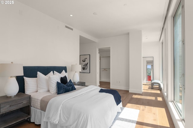 bedroom with wood finished floors, a walk in closet, and baseboards