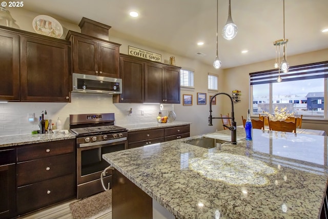 kitchen with a center island with sink, a sink, light stone counters, tasteful backsplash, and stainless steel appliances